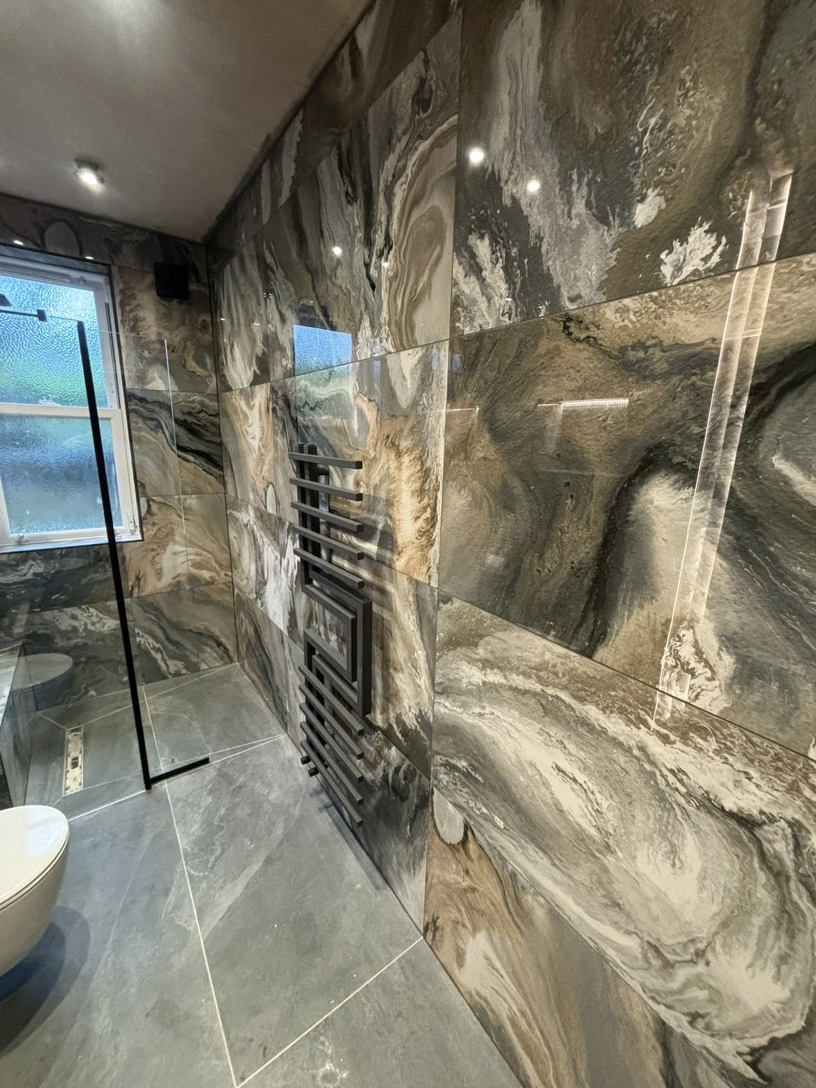 Marble-effect porcelain wall tiling with black designer heated towel rail and linear shower drain