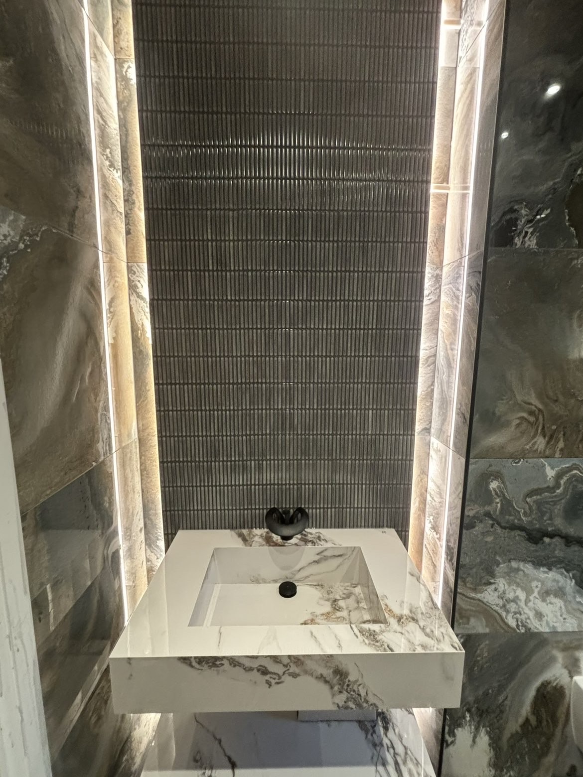 Floating stone basin with matt black wall-mounted tap against fluted tiling with LED strip lighting