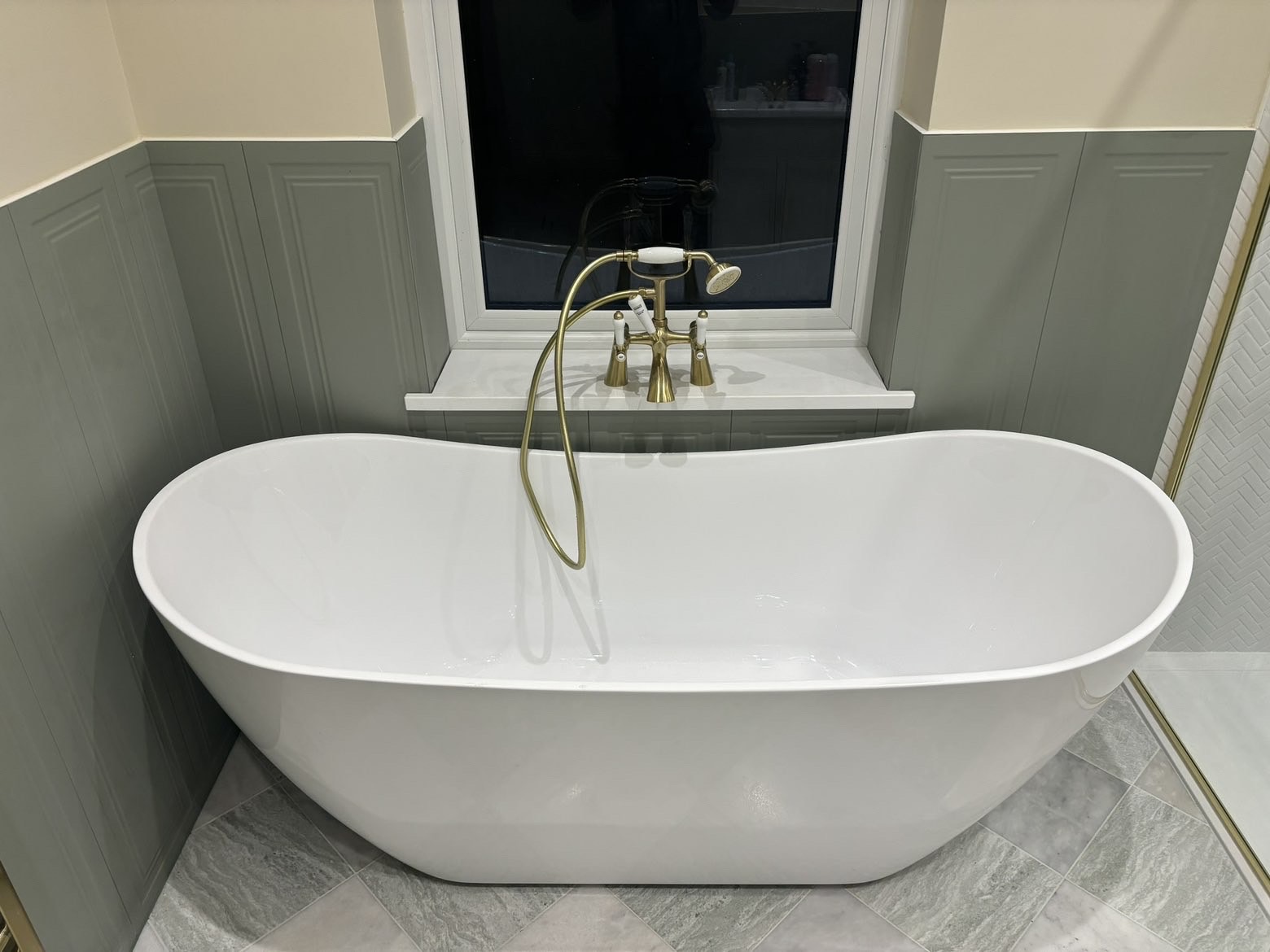 Freestanding slipper bath beneath a window with brushed brass deck-mounted bath shower mixer and handset
