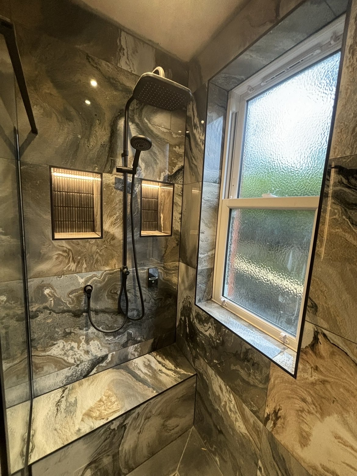 Wet-room shower area with black rainfall shower, handset and two LED-lit recessed niches